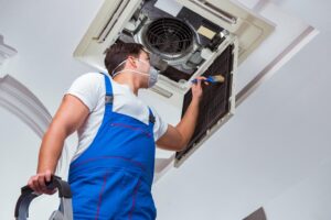 An AC technician is cleaning the AC fan installed on the ceiling.